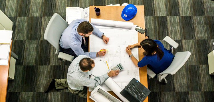Three people discussing over architectural blueprints at a table